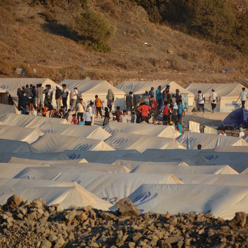 Migrants are seen alongside white tents inside the new temporary refugee camp in Kara Tepe, Greece.
