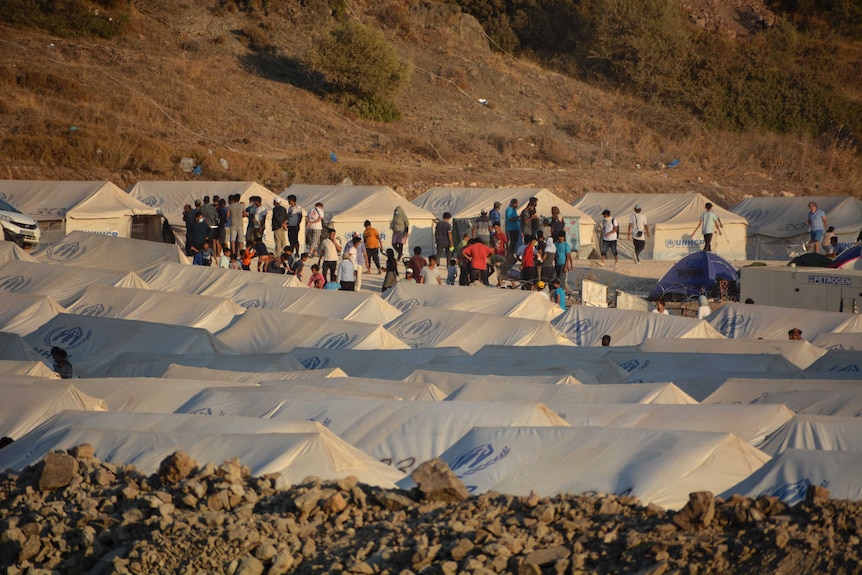 Migrants are seen alongside white tents inside the new temporary refugee camp in Kara Tepe, Greece.