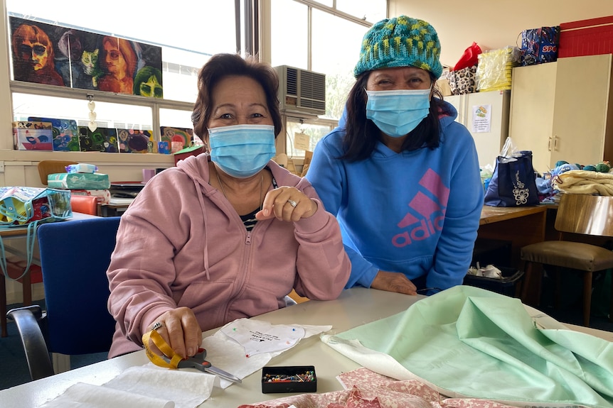 Two women with face masks sitting in front of sewing supplies