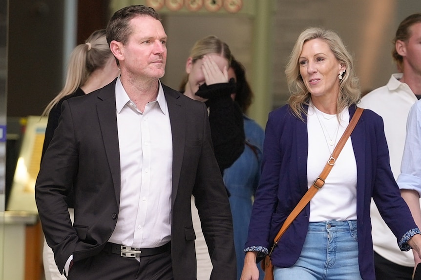 a man in a balck suit leaving court with a blonde woman beside him