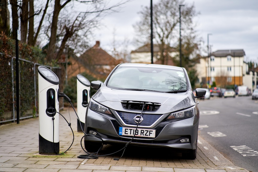 A car parked on a suburban street with a cable plugged into the front