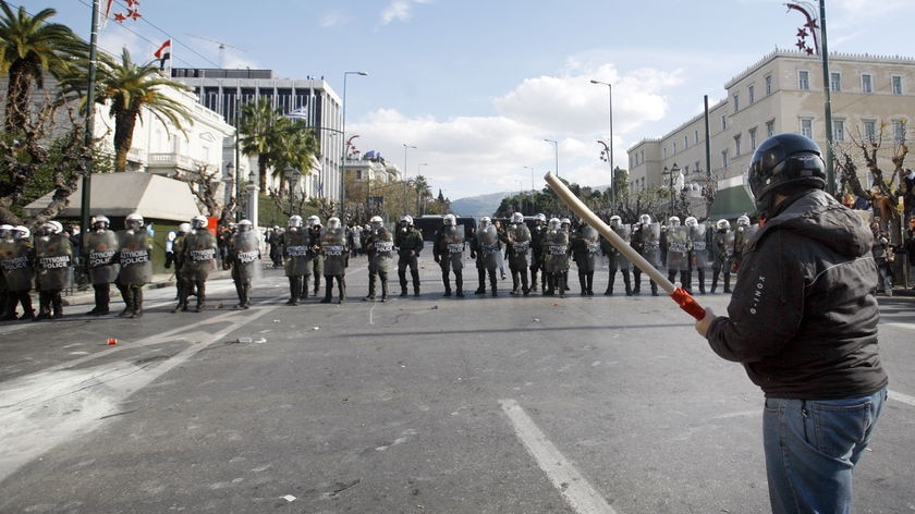 A father stands in front of riot police during a demonstration outside the Greek Parliament.