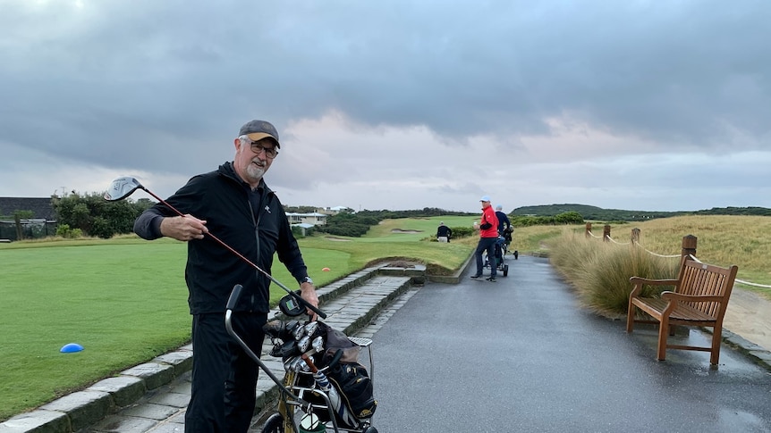 A man pulls a golf club out of his bag as he stands on a footpath at the Barwon Heads Golf Club.