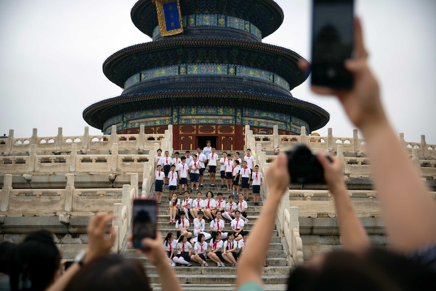 A group of Chinese children sitting and standing in front of an traditional building in Beijing.