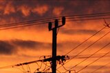 Silhouette of a power pole with many lines with red sunrise behind
