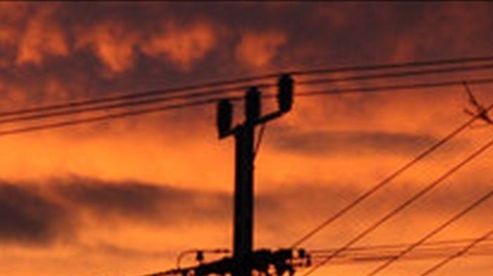 Silhouette of a power pole with many lines with red sunrise behind