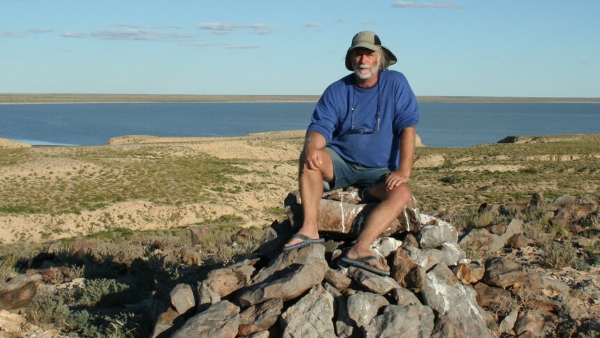 man sitting on rocks in front of desert lake