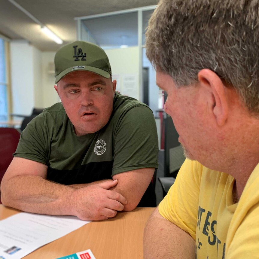 Kevin Maloney sits facing the camera at a table with Michael Mayne who is looking back at him.