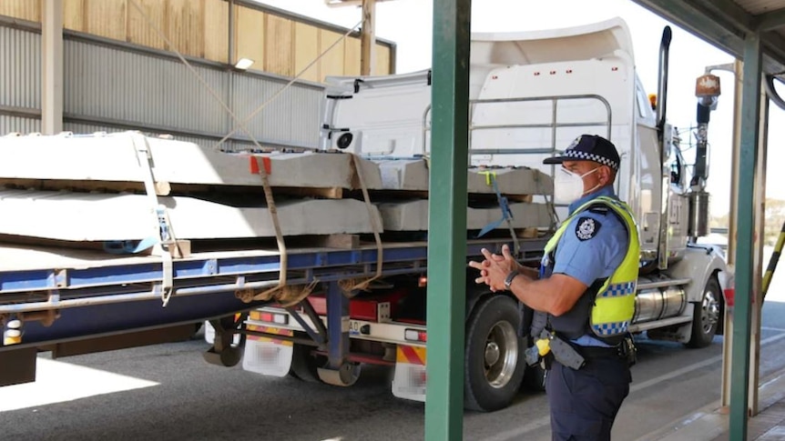 A police officer wearing a mask stands under a shed-like structure next to a truck at the Eucla border checkpoint.