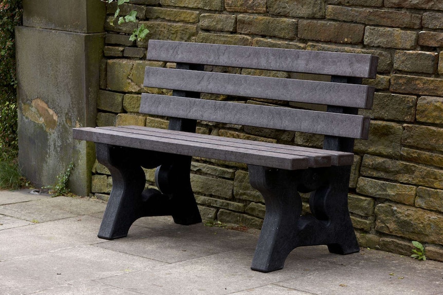 A plastic park bench next to a stone wall.