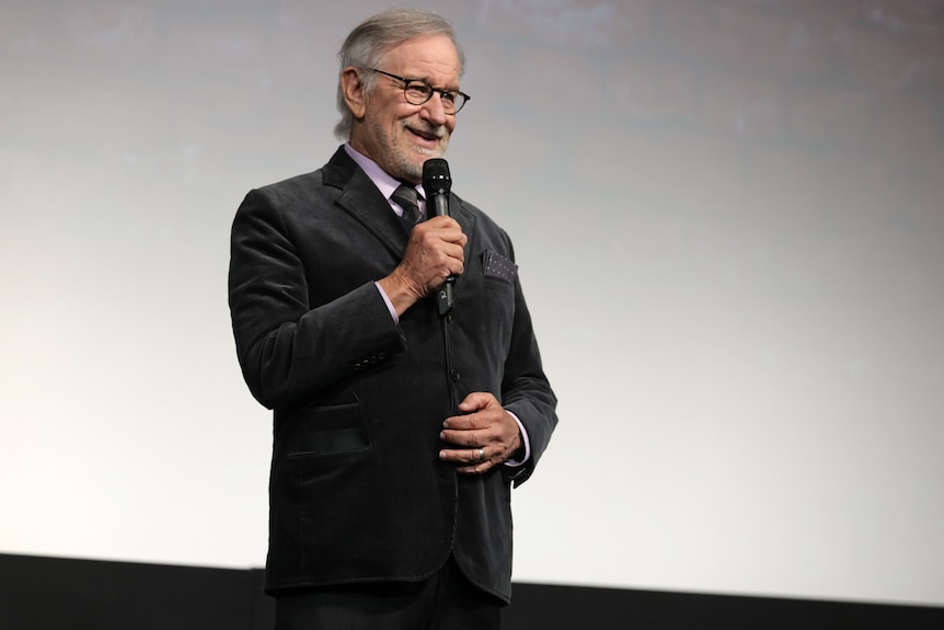 Steven Spielberg holding a microphone, dressed in a suit