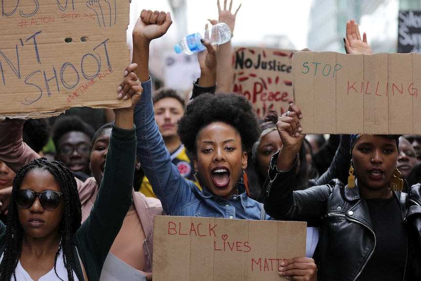 Demonstrators from the Black Lives Matter movement march with fists raised and cardboard signs.