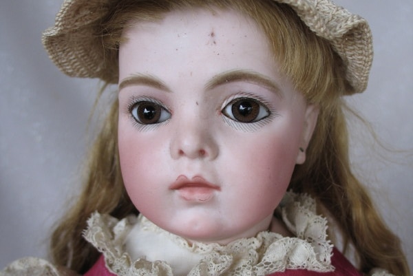 An antique doll wearing a woven hat and pink dress with lace trim.