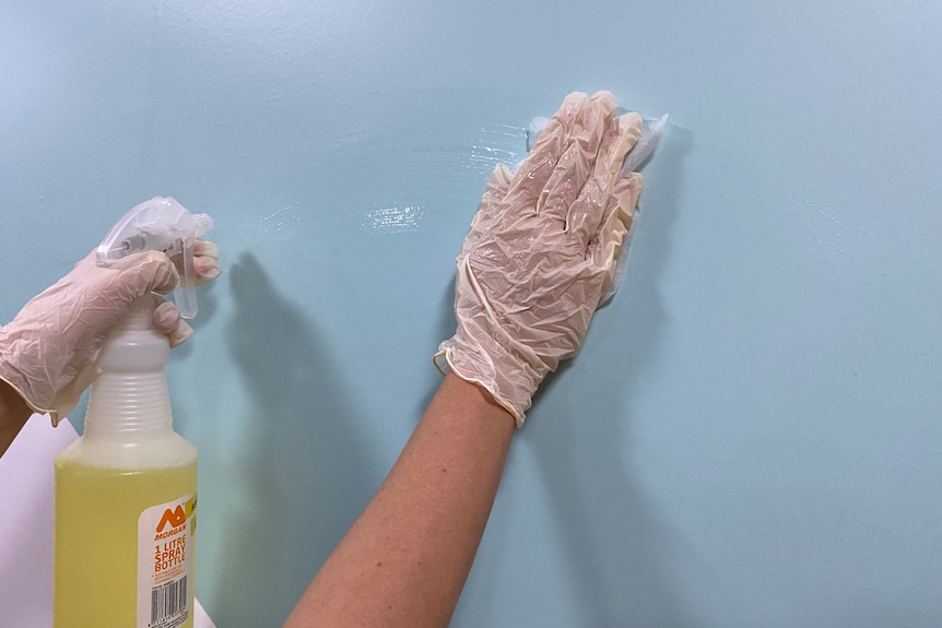 Gloved hands work to clean a wall.