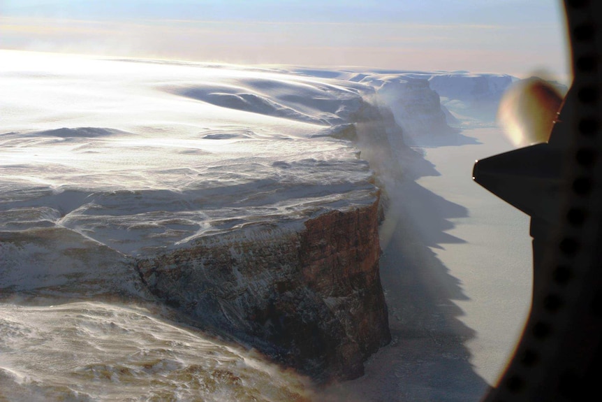 Petermann Glacier's east wall near the terminus of the floating ice shelf with blowing snow from the east