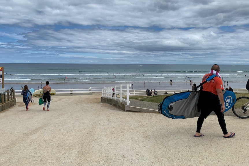 Surfers and swimmers on a beach under a cloudy blue sky.