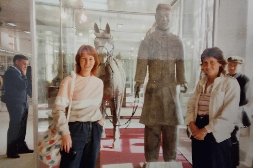 Two young women standing in front of a display of terracotta sculptures
