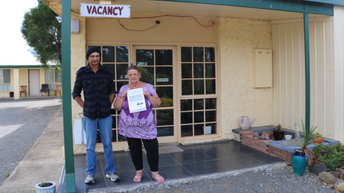 Carol and Robert Soewardie stand outside the reception of their motel near a "vacancy" sign holding papers