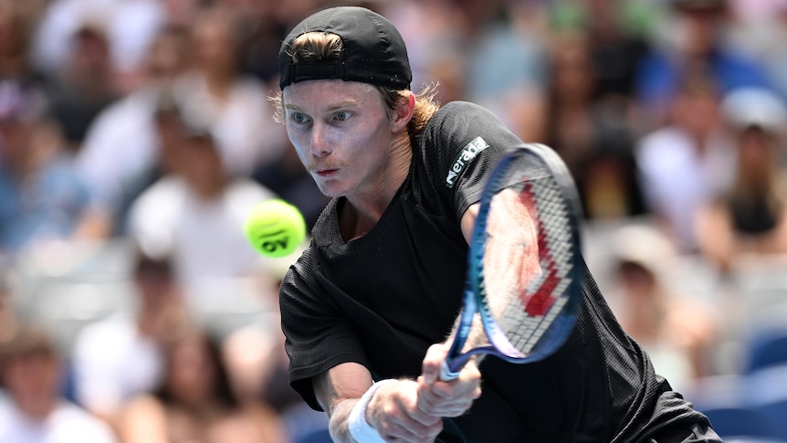 An Australian male tennis player hits a double-fisted backhand at the 2024 Australian Open.