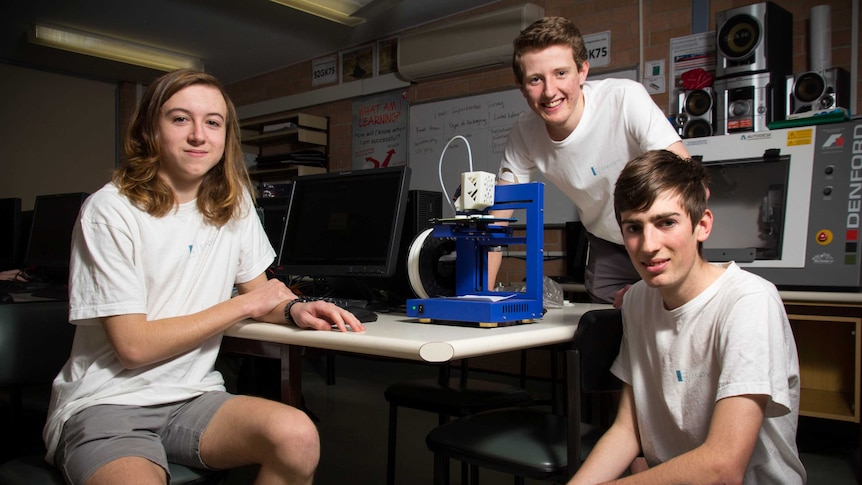 Connor Minchinton, Liam Whiteley, and Daniel Lambkin kneel next to a 3D printer.