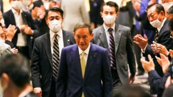 Yoshihide Suga walking in a room filled with men wearing face masks