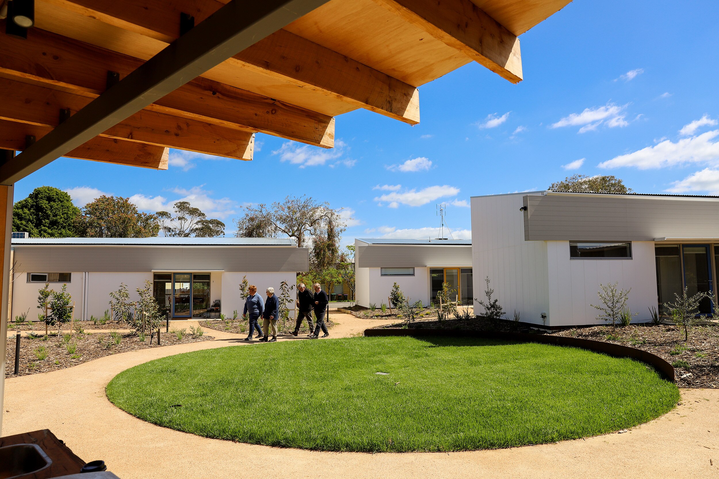 A group walks through a grassed space encircled by a path surrounded by modern units