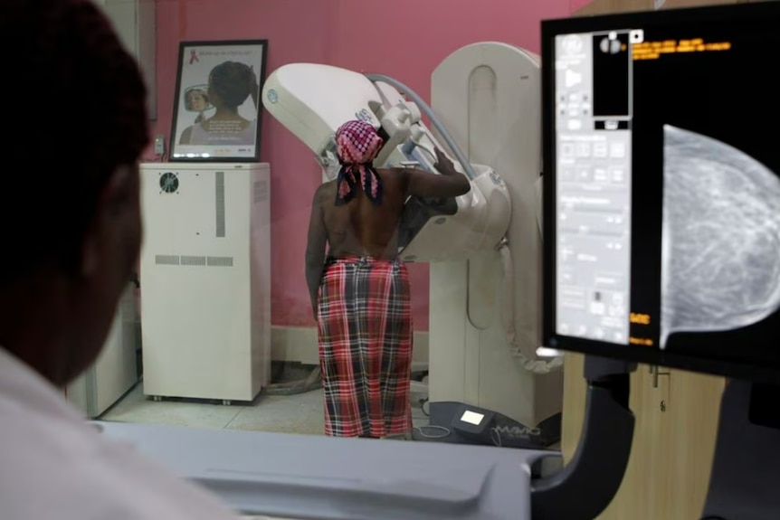 A patient is seen through the glass as she undergoes a mammogram X-ray 