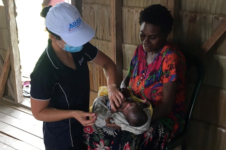 a nurse wearing a navy YWAM polo shirt tends to a baby on a woman's lap