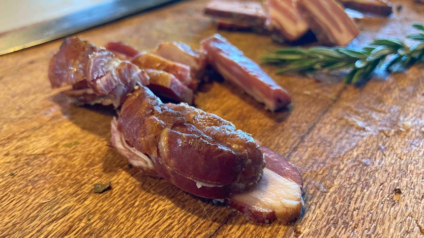 A close-up shot of cuts of red meat on a wooden shopping board beside a sprig of rosemary.