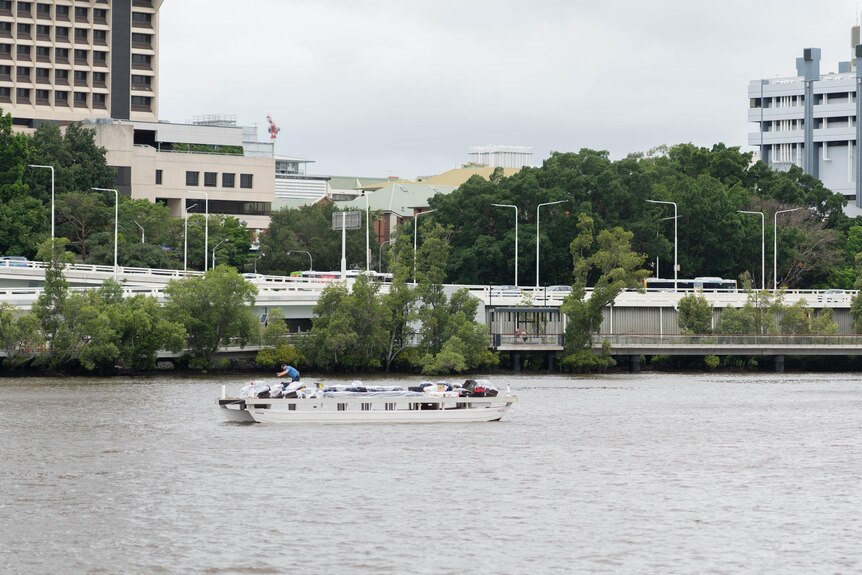 Un homme vérifiant quelque chose sur un bateau au milieu d'une rivière entourée d'immeubles de grande hauteur.