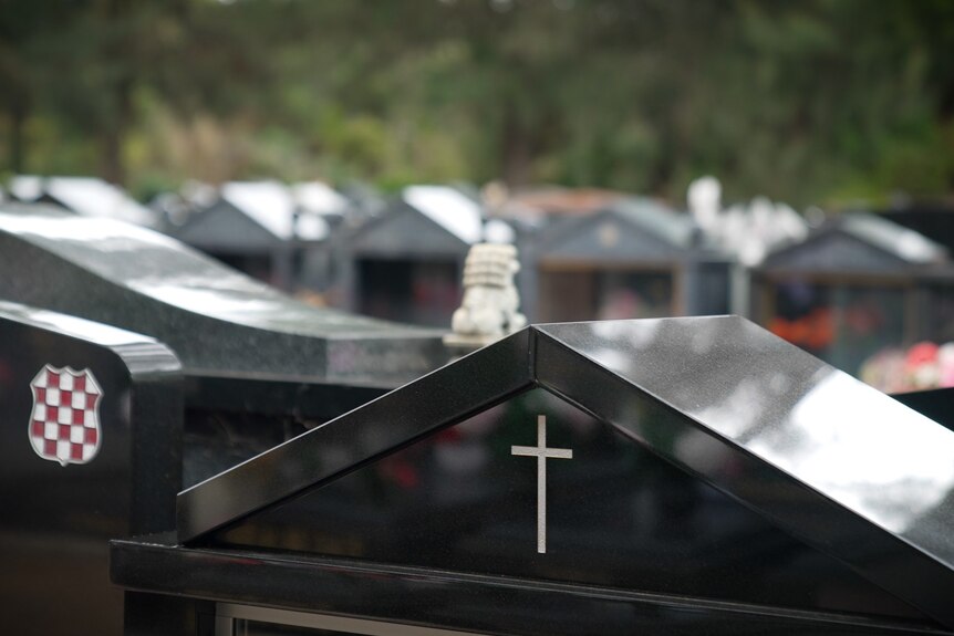 A crucifix on a grave stone in the foreground, amid many other grave stones.