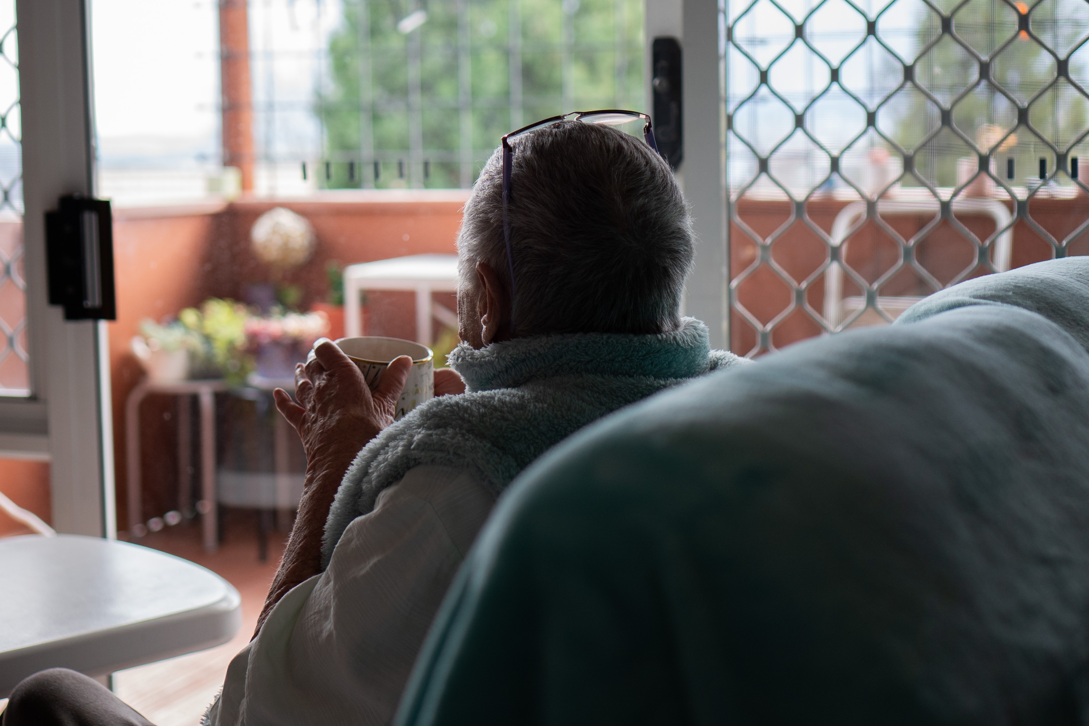 An elderly woman sits a cup of tea. Her face is not visible.