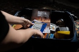 An open suitcase with a torch and bushfire guide inside; hands place will
