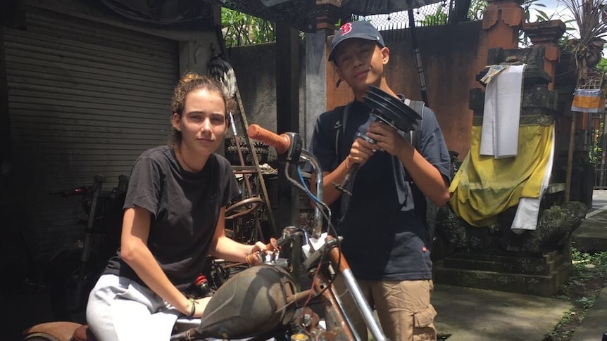 A young girl on a motorcycle with a boy teenager standing beside her.