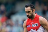 Adam Goodes, in his red-and-white Swans guernsey, looks down at the ground.