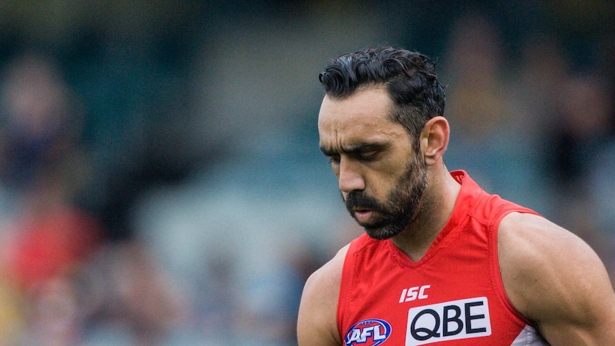 Adam Goodes, in his red-and-white Swans guernsey, looks down at the ground.