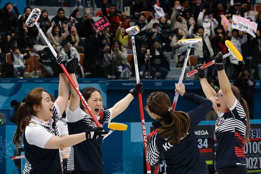 Four members of South Korea's curling team raise their sticks in the air in celebration.