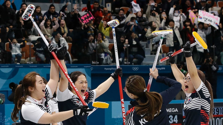 Four members of South Korea's curling team raise their sticks in the air in celebration.