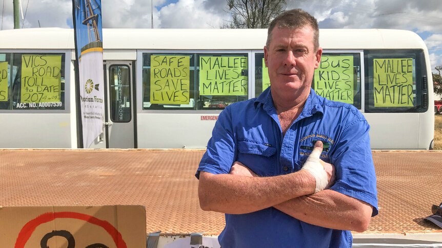 Peter Thompson crosses his arms while standing in front of a bus decorated with protest signs including "Mallee Lives Matter".