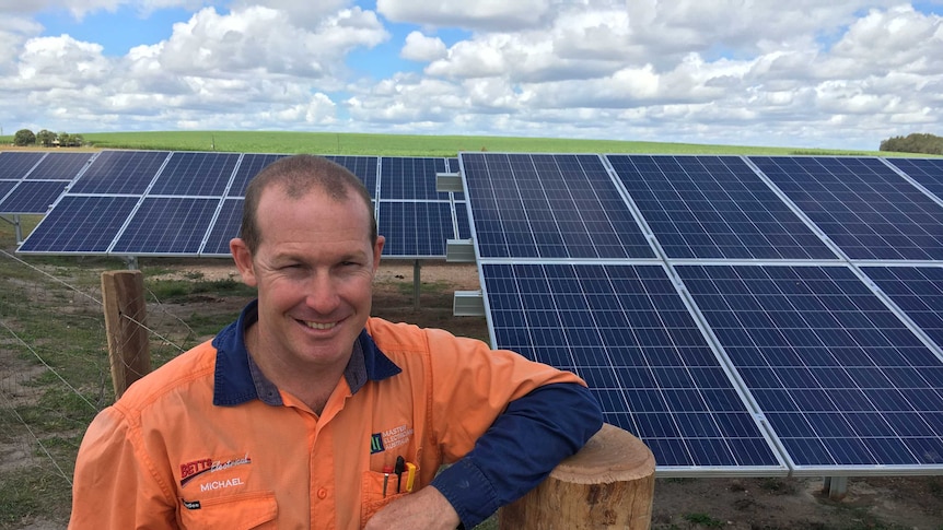 Electrician Michael Betts stands in front of solar panels on a Queensland farm.