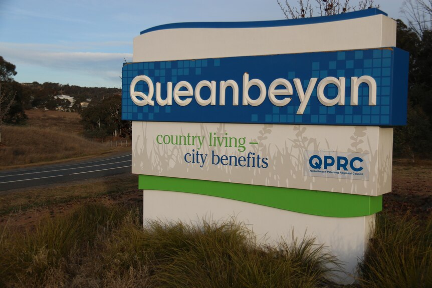 A sign that says Queanbeyan with words 'country living city benefits' written on it 