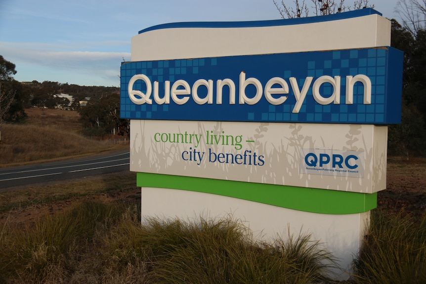 Un panneau indiquant Queanbeyan avec les mots « avantages de la ville à la campagne » écrit dessus 