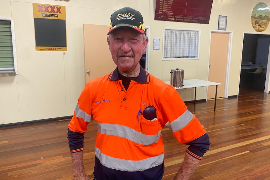 Man standing in a town hall in orange high vis shirt with a black cap