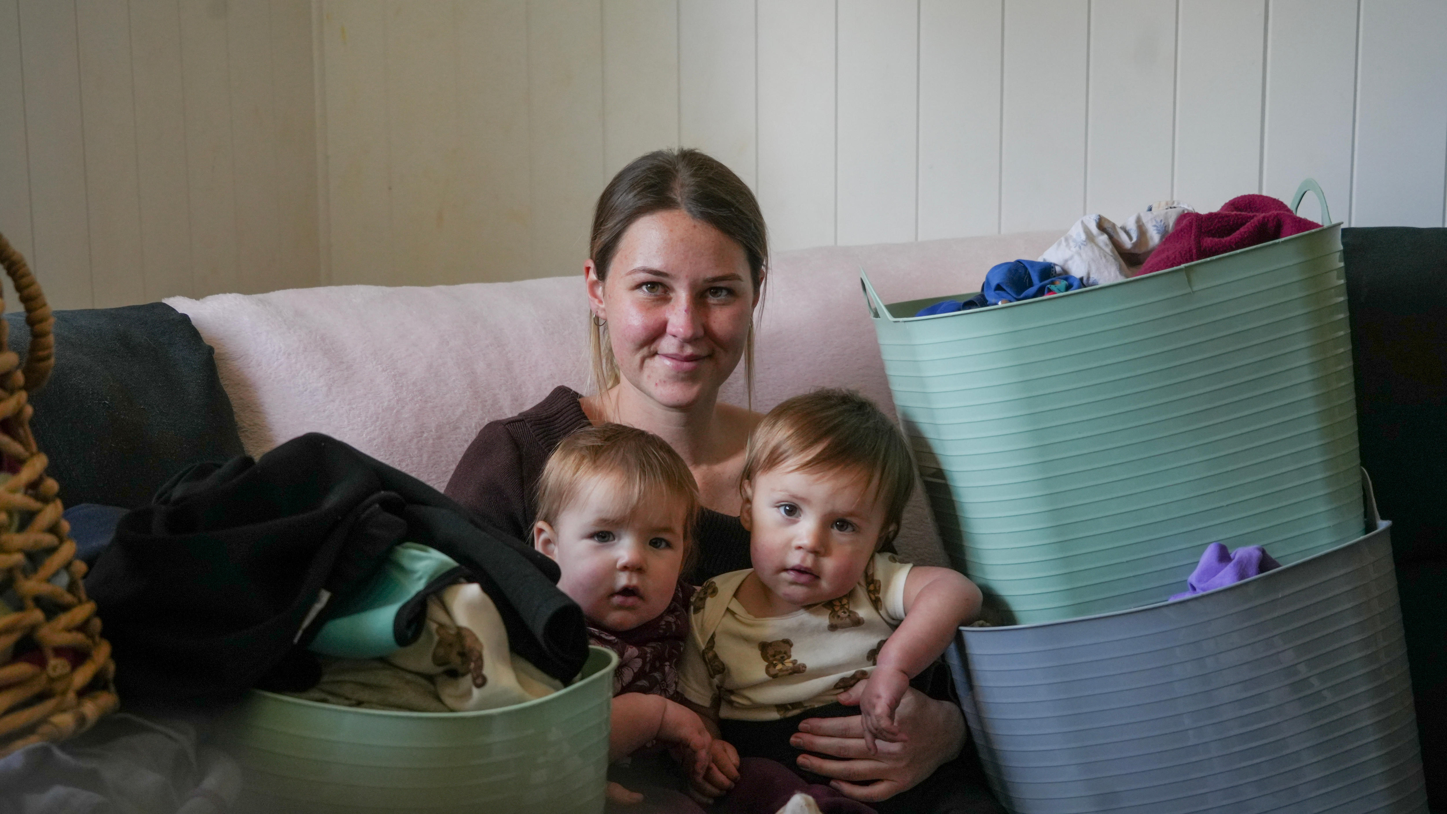 young woman with two toddlers on her lap, surrounded with baskets of laundry