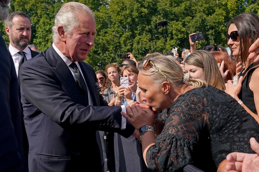 A well-wisher kisses the hand of Britain's King Charles III as he walks outside at Buckingham Palace