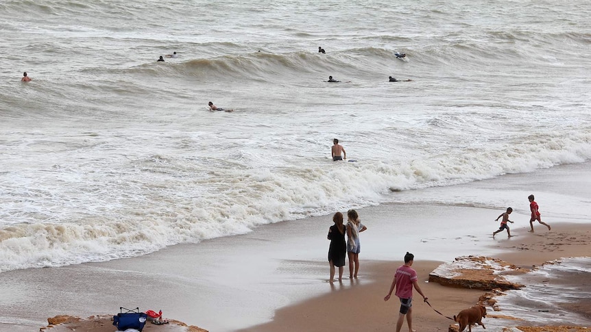 A high-angle shot of surfers getting into the water as bystanders and children watch from the shore.