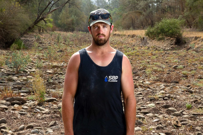 A man is a blue singlet stands in a dry creek bed.