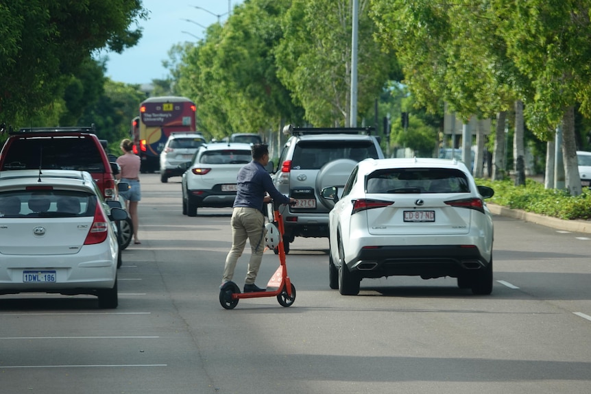 A man crossing the road on a scooter behind several vehicles