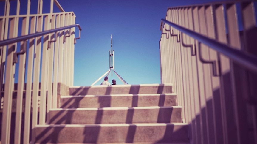 The top of Parliament House in Canberra is visible at the top of a staircase, half in shadow. There are unidentified two people