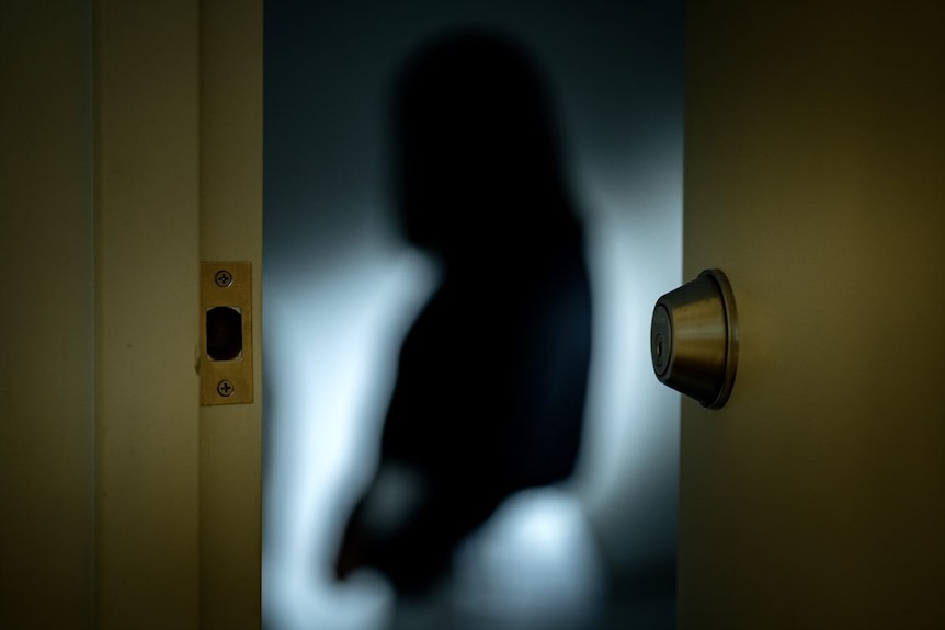 A blurred woman stands in a room. A door is swinging shut. 
